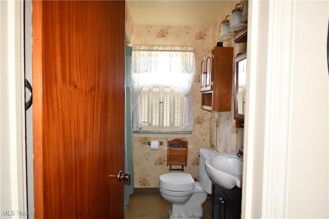 bathroom featuring a sink, toilet, and wallpapered walls