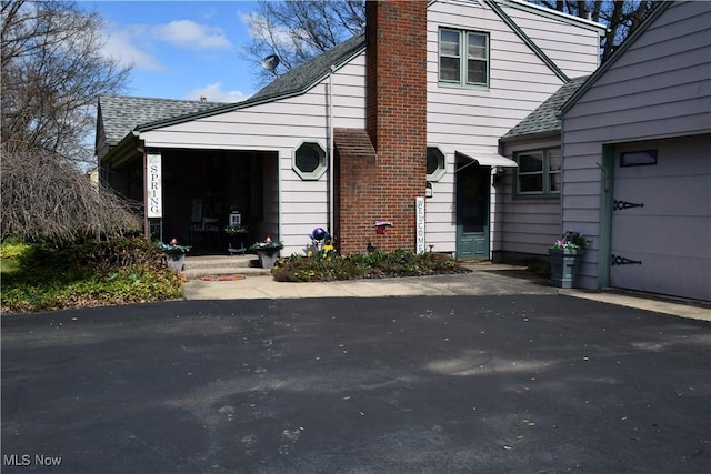 view of property exterior with a garage, a shingled roof, and a chimney