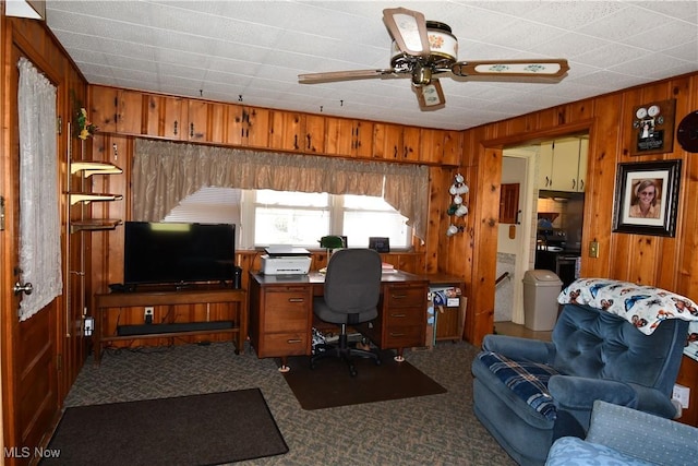 carpeted home office with ceiling fan and wood walls