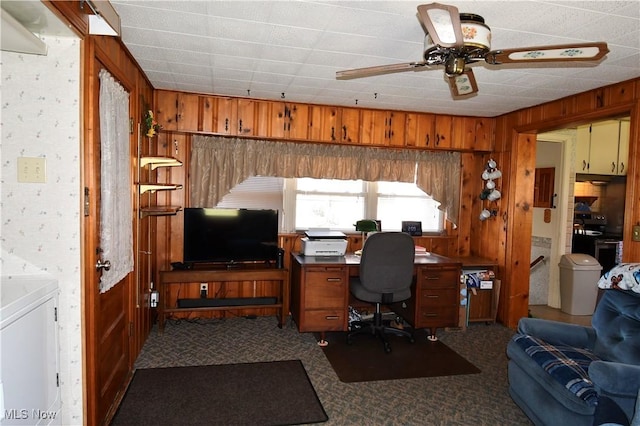 carpeted home office with ceiling fan and wooden walls