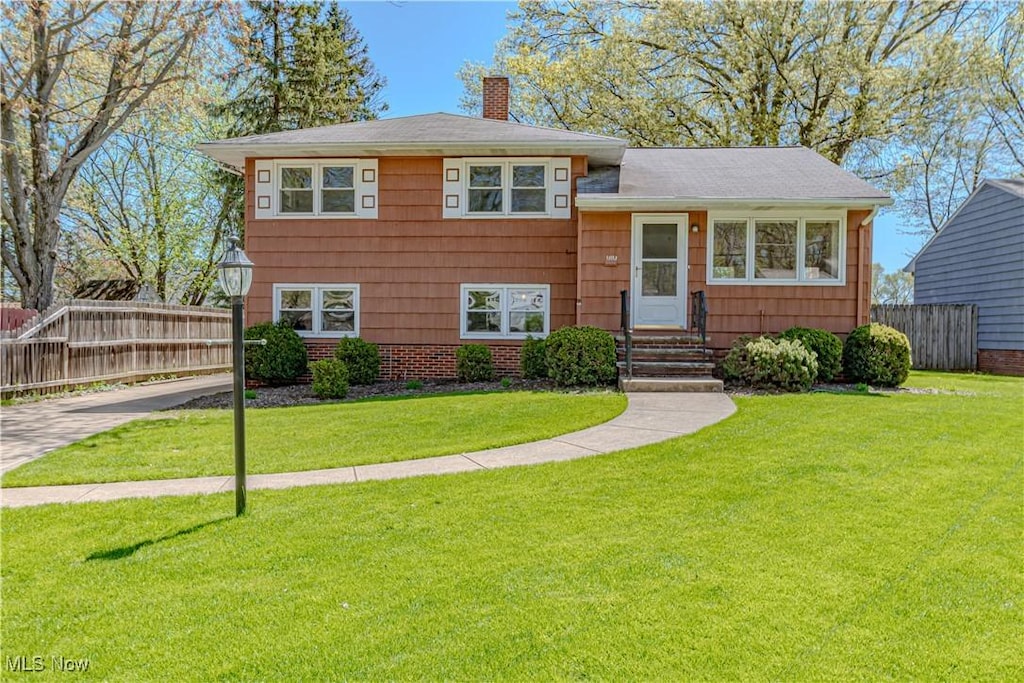 split level home with a chimney, fence, and a front lawn