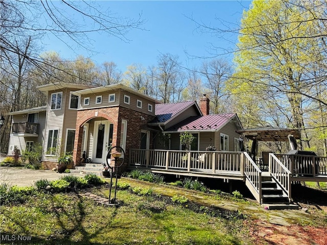 view of front of property featuring a chimney, metal roof, and brick siding