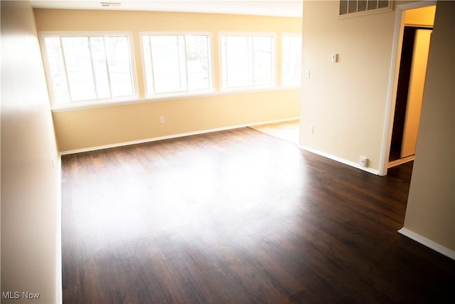 unfurnished room featuring dark wood-style flooring, baseboards, and visible vents