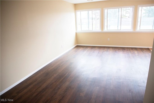 spare room featuring plenty of natural light, baseboards, and dark wood-style floors