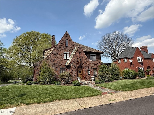 tudor house with brick siding, a chimney, and a front yard