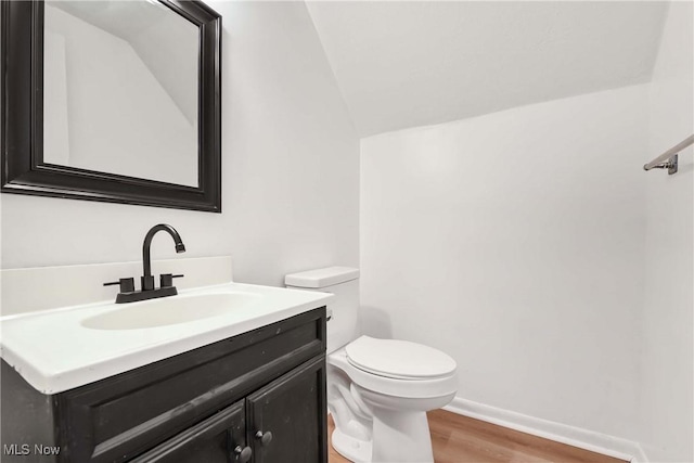 bathroom featuring vanity, toilet, baseboards, wood finished floors, and lofted ceiling