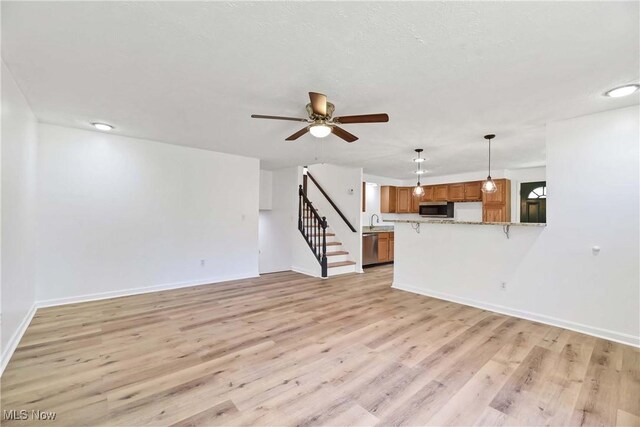 unfurnished living room featuring ceiling fan, stairway, baseboards, a sink, and light wood-style floors