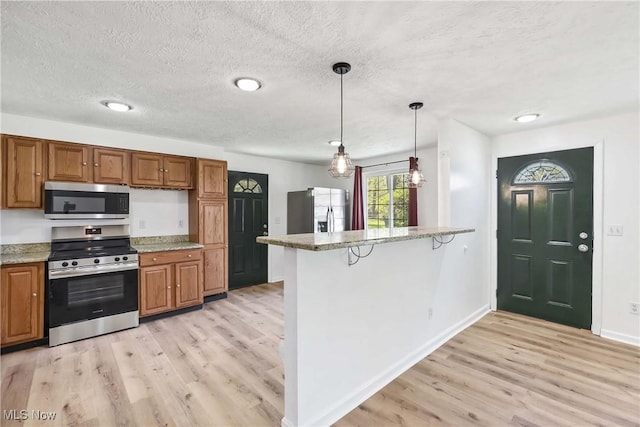 kitchen featuring light wood-style floors, stainless steel appliances, brown cabinets, and a textured ceiling