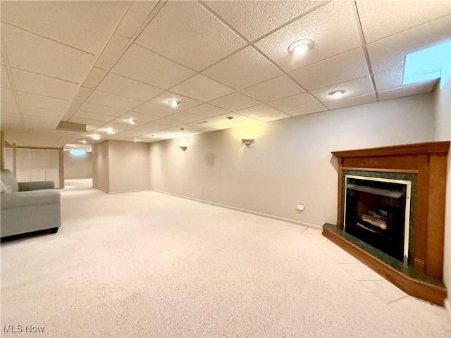 unfurnished living room with carpet floors, a fireplace with raised hearth, a paneled ceiling, and baseboards