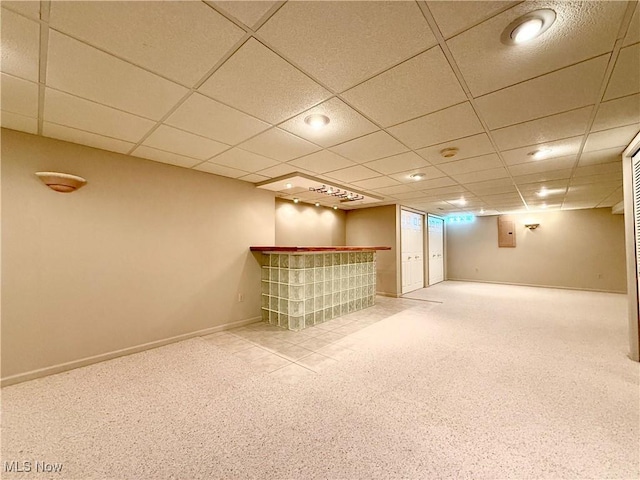finished basement featuring carpet floors, baseboards, a drop ceiling, and a dry bar