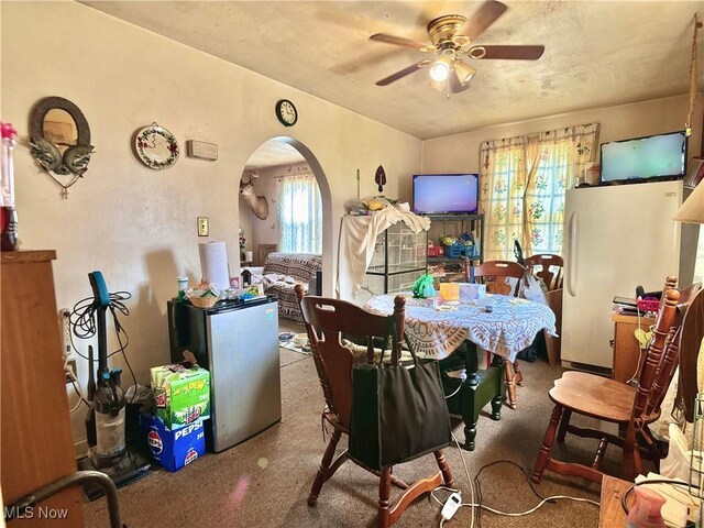 carpeted dining room featuring arched walkways and ceiling fan