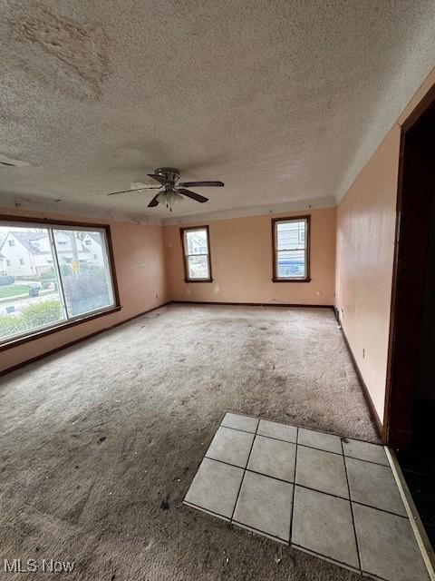 carpeted spare room featuring baseboards, a ceiling fan, and a textured ceiling