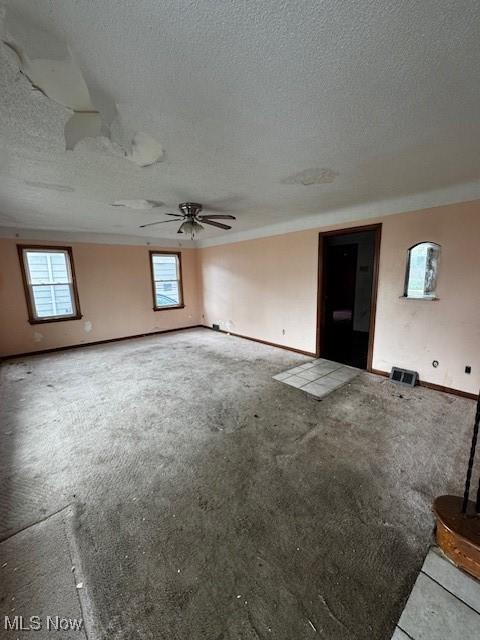 unfurnished living room with carpet flooring, a textured ceiling, baseboards, and ceiling fan