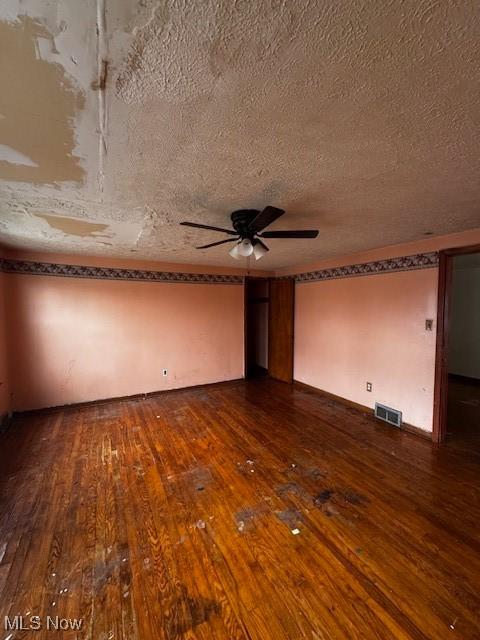 unfurnished room with visible vents, a ceiling fan, a textured ceiling, and dark wood-type flooring
