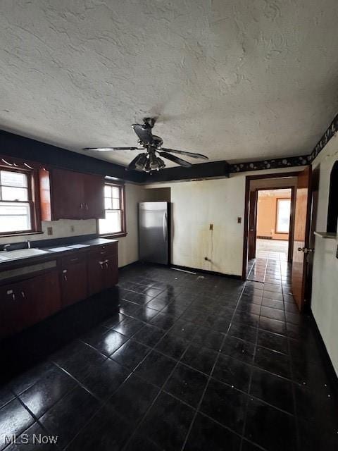 kitchen with freestanding refrigerator, a sink, dark countertops, and dark tile patterned flooring
