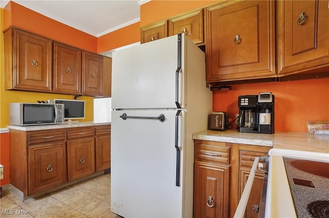 kitchen featuring crown molding, freestanding refrigerator, stainless steel microwave, and brown cabinets