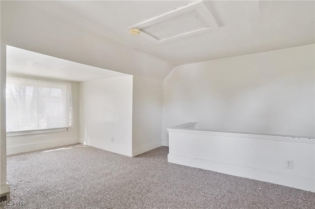 spare room with vaulted ceiling, carpet floors, baseboards, and attic access