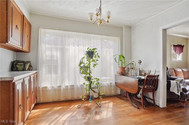 dining space with light wood-style floors, ornamental molding, a notable chandelier, and a healthy amount of sunlight