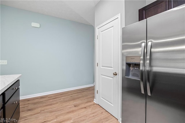 kitchen featuring dark brown cabinetry, baseboards, stainless steel refrigerator with ice dispenser, light wood-type flooring, and light stone counters