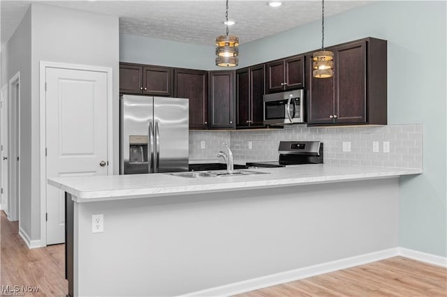 kitchen featuring appliances with stainless steel finishes, dark brown cabinets, a sink, light countertops, and a peninsula