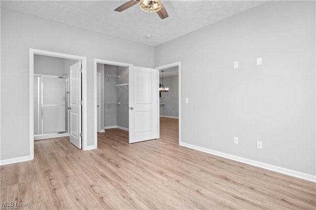 unfurnished bedroom with a closet, baseboards, a spacious closet, light wood finished floors, and ceiling fan with notable chandelier