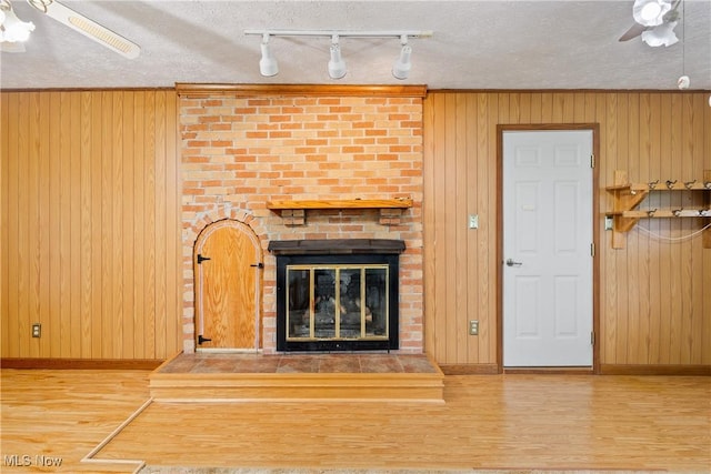 unfurnished living room with ceiling fan, a fireplace, wood walls, wood finished floors, and baseboards