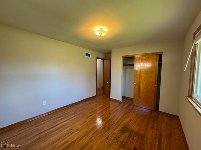 unfurnished bedroom featuring baseboards, visible vents, wood finished floors, and a closet