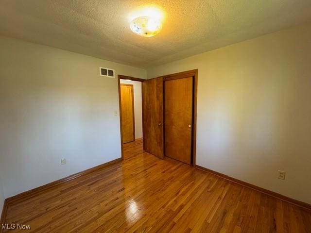 unfurnished bedroom with baseboards, visible vents, wood finished floors, and a closet