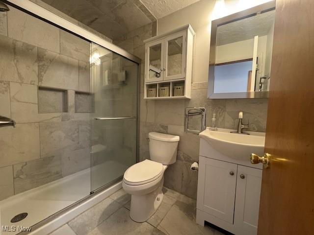 bathroom with tile walls, a stall shower, vanity, tile patterned floors, and toilet