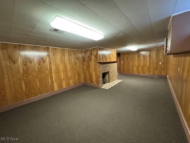 finished basement featuring visible vents, wood walls, a fireplace, baseboards, and carpet flooring
