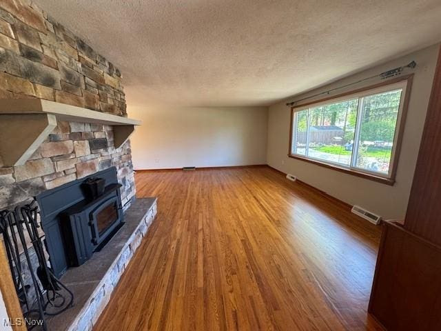 unfurnished living room featuring a textured ceiling, baseboards, wood finished floors, and visible vents