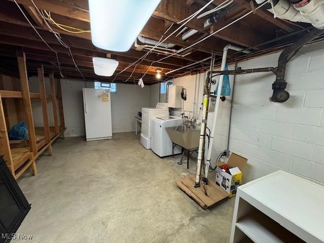below grade area featuring freestanding refrigerator, a sink, and washer and clothes dryer