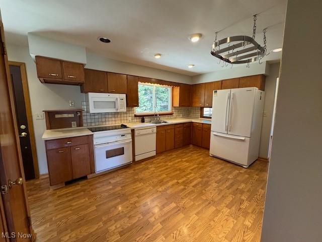 kitchen featuring tasteful backsplash, a sink, light countertops, white appliances, and light wood-style flooring