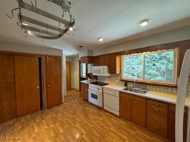 kitchen featuring brown cabinets, a sink, white appliances, light countertops, and tasteful backsplash