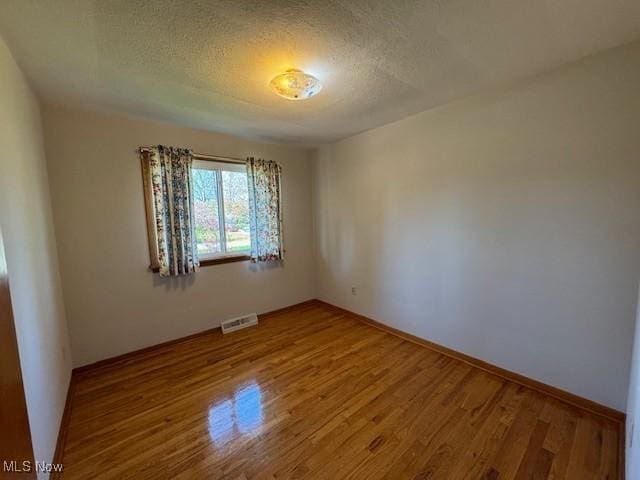 empty room with baseboards, a textured ceiling, visible vents, and wood finished floors