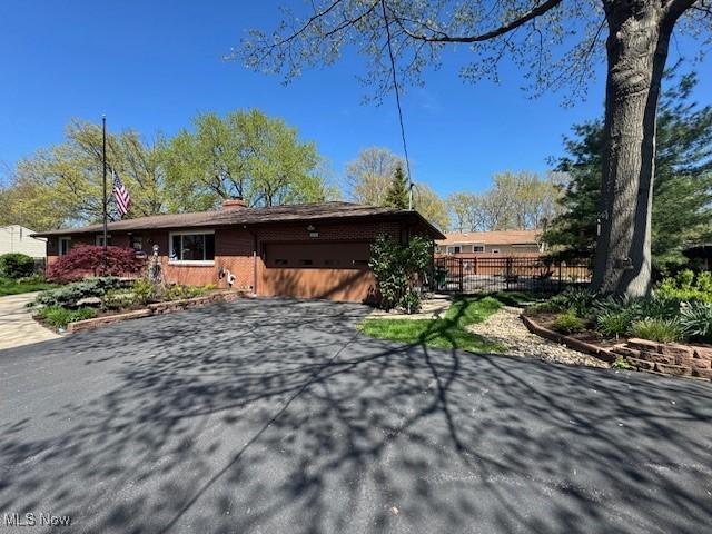 exterior space featuring brick siding, an attached garage, fence, and aphalt driveway