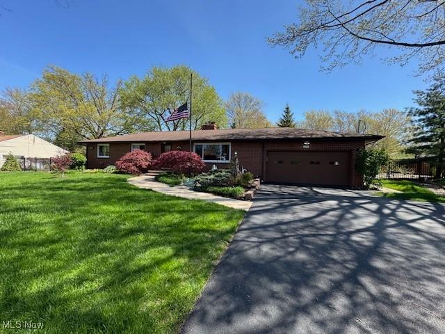ranch-style house with aphalt driveway, a chimney, fence, a front lawn, and an attached garage