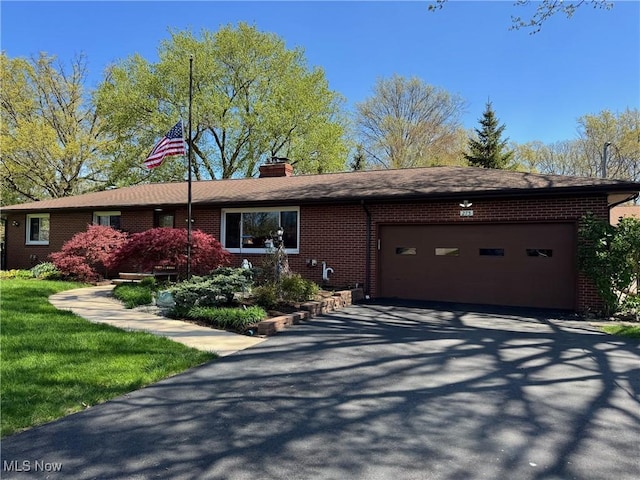 single story home featuring brick siding, an attached garage, a chimney, and aphalt driveway