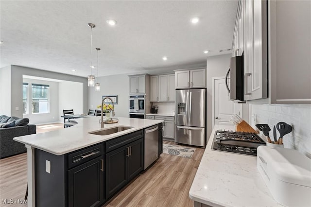 kitchen with decorative light fixtures, appliances with stainless steel finishes, a sink, light wood finished floors, and open floor plan