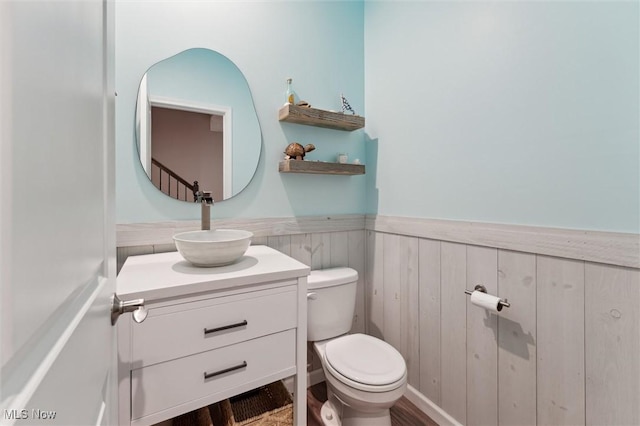 half bath featuring vanity, a wainscoted wall, and toilet