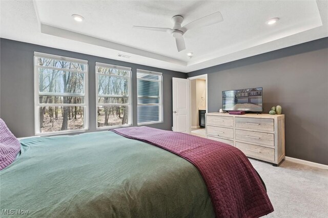 bedroom with ceiling fan, visible vents, light colored carpet, baseboards, and a tray ceiling