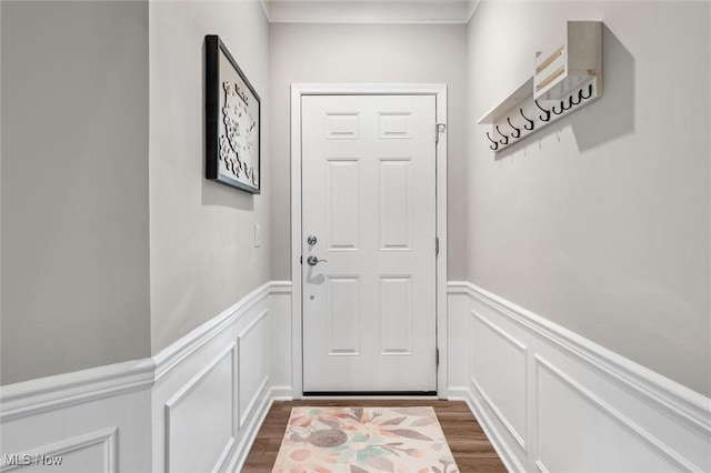 doorway to outside featuring crown molding, a wainscoted wall, a decorative wall, and dark wood finished floors