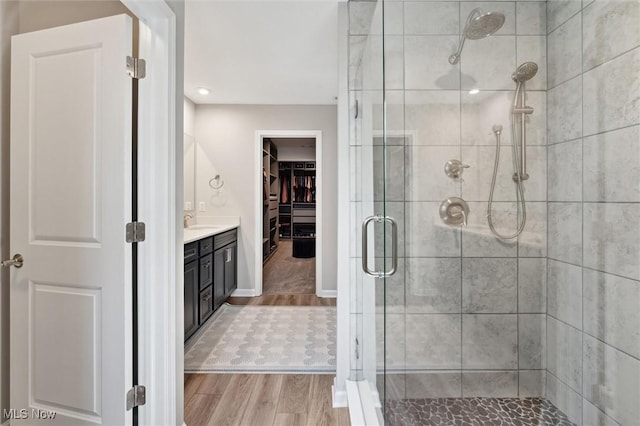 bathroom with a walk in closet, vanity, baseboards, a shower stall, and wood finished floors