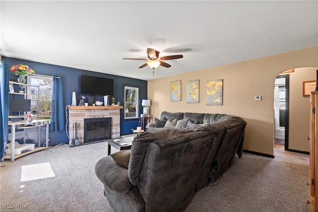 carpeted living area featuring baseboards, arched walkways, a fireplace with flush hearth, and a ceiling fan