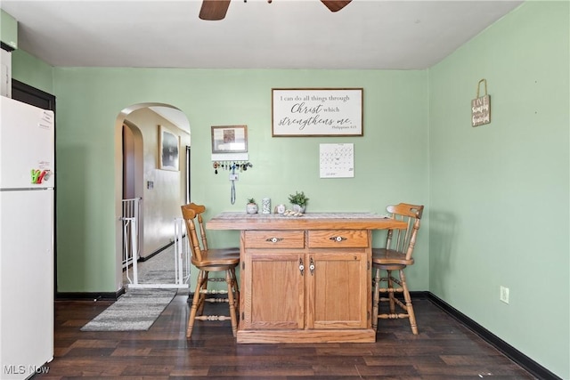 dining room featuring arched walkways, ceiling fan, baseboards, and dark wood-type flooring