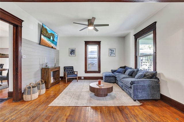 living room featuring baseboards, a ceiling fan, wood finished floors, and a wealth of natural light