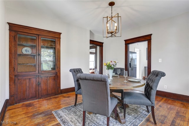 dining space with baseboards, hardwood / wood-style floors, and an inviting chandelier