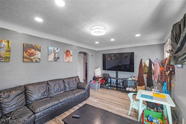 living area with recessed lighting, arched walkways, a textured ceiling, and wood finished floors