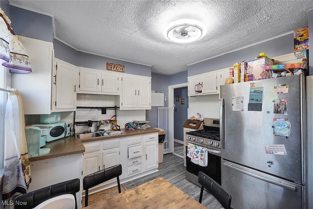 kitchen with dark wood-type flooring, white cabinetry, a textured ceiling, a sink, and appliances with stainless steel finishes