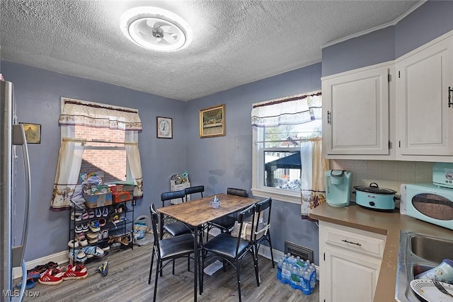 dining area with visible vents, a textured ceiling, light wood finished floors, and baseboards